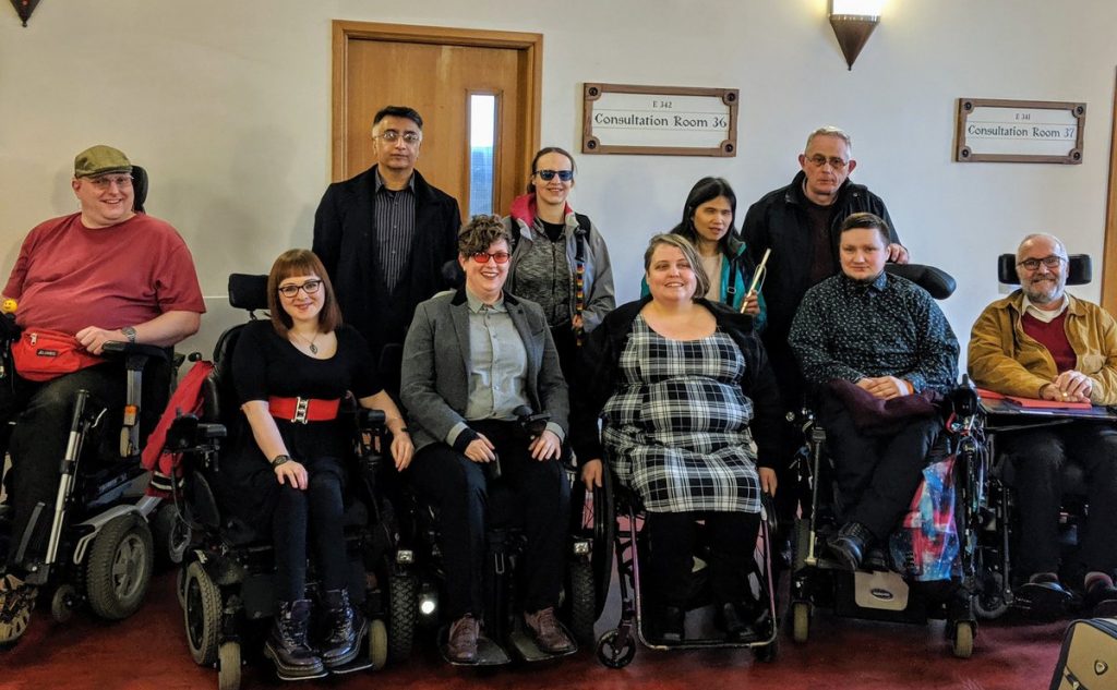 Photograph of Esther and 9 of her supporters (6 using wheelchairs, one with a symbol cane and two wearing coloured lenses) outside the courtroom.